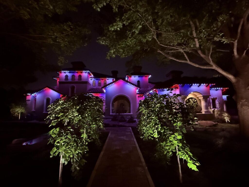 Home with landscape tree uplighting and purple permanent roofline lights