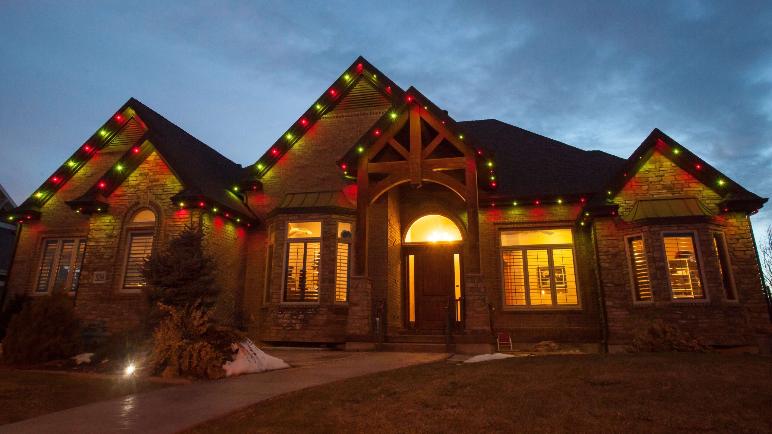 Game day red and gold stone home dusk with permanent outdoor lighting