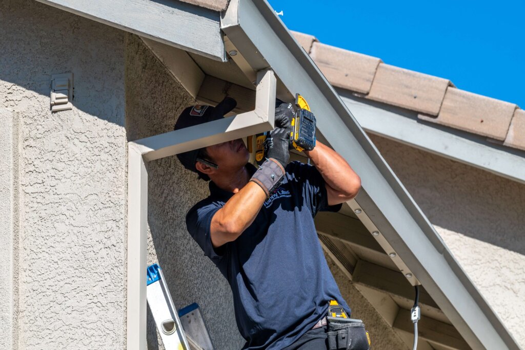Happy Lites technician drilling to mount permanent light track under an eave