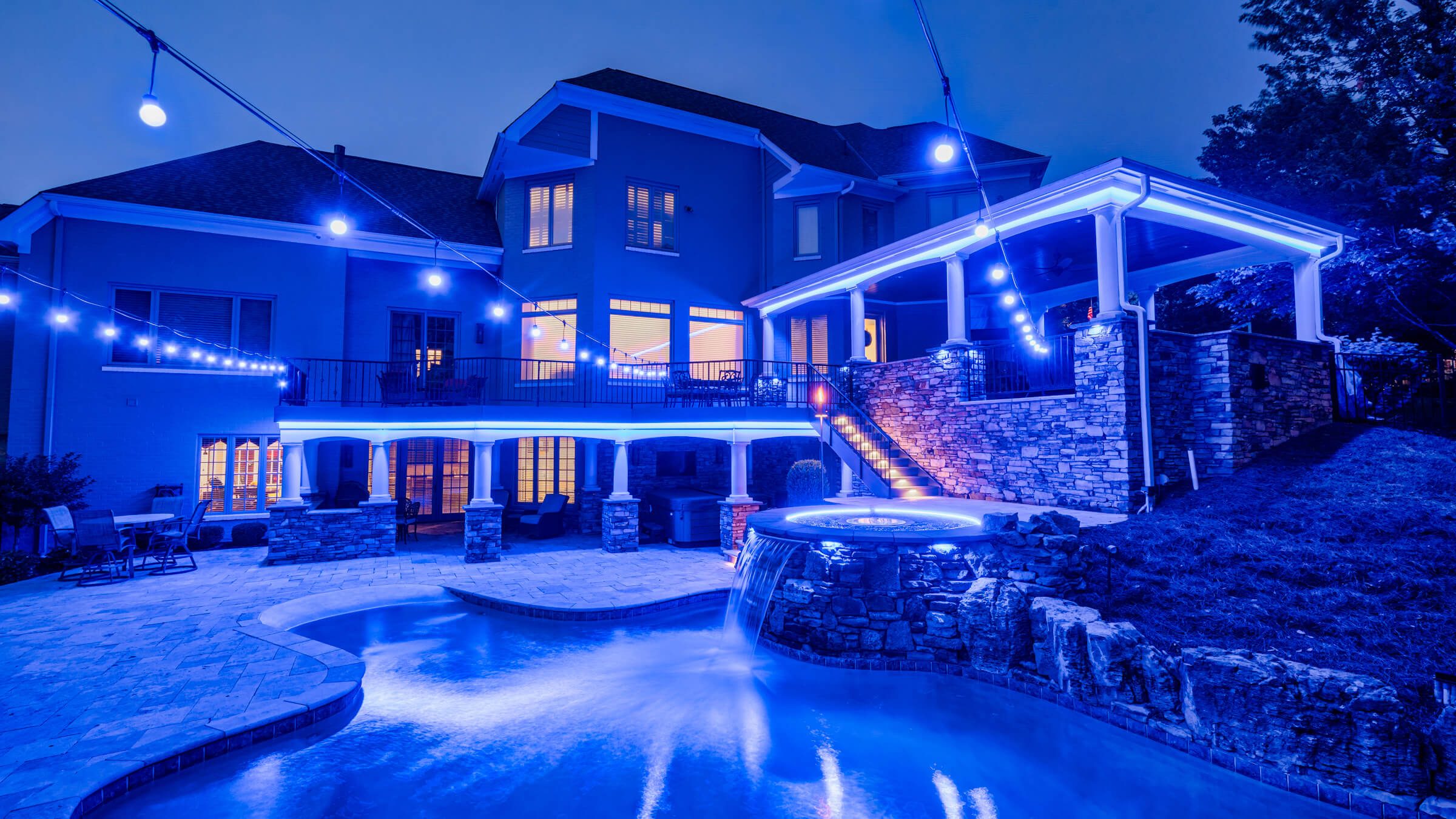 Backyard pool, patio and trees with blue pool deck permanent outdoor lighting