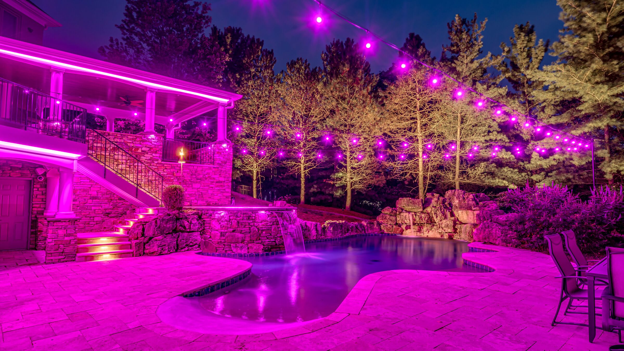 Backyard pool, patio and trees with magenta permanent outdoor lighting