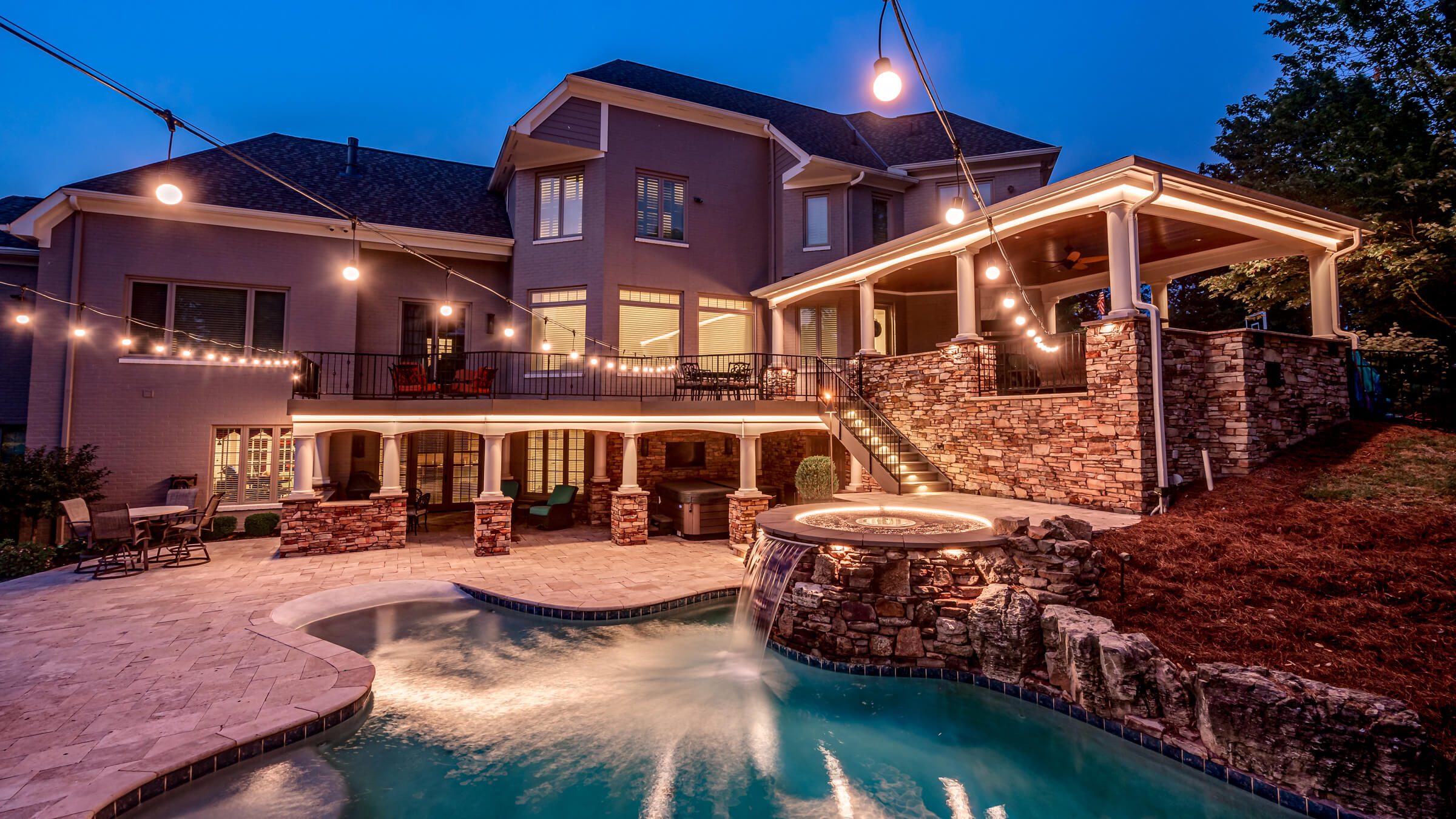 Backyard pool, patio and trees with pool deck multicolor at dusk permanent outdoor lighting