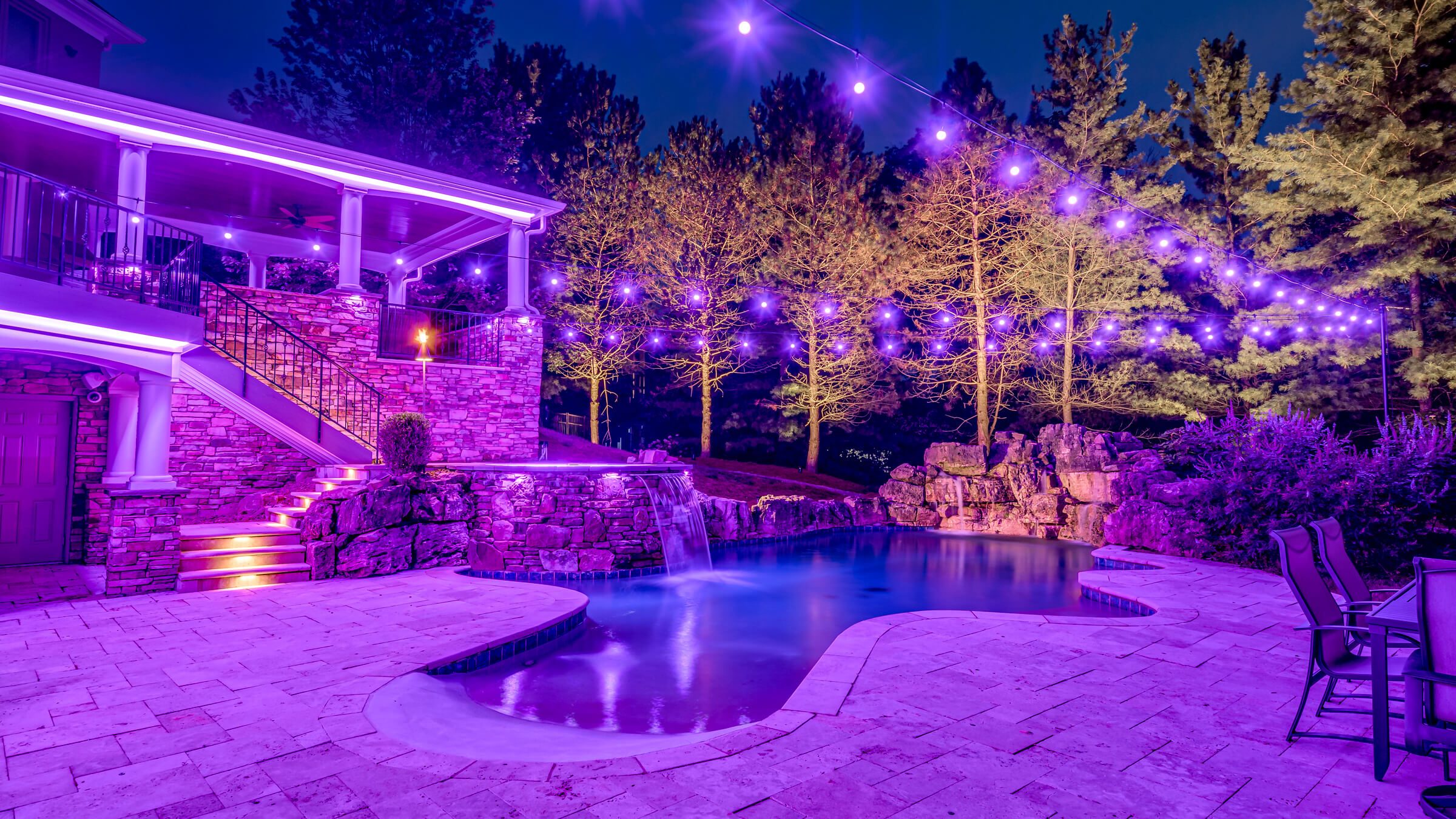 Backyard pool, patio and trees with purple permanent outdoor lighting