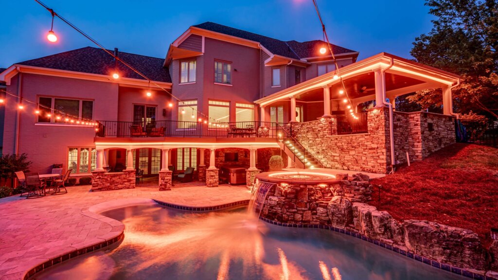 Backyard pool, patio and trees with red and orange permanent outdoor lighting