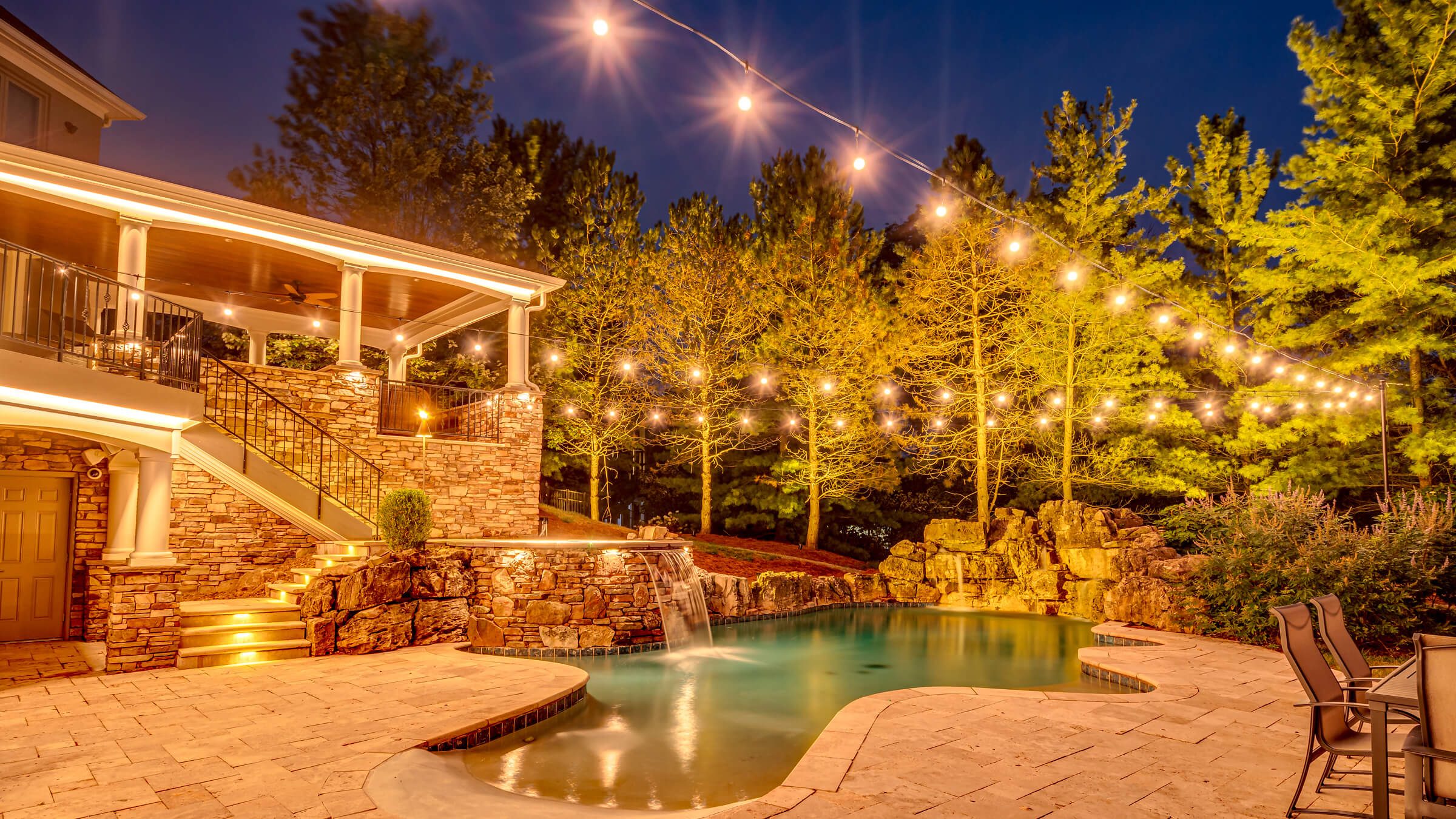 Backyard pool, patio and trees with warm amber permanent outdoor lighting
