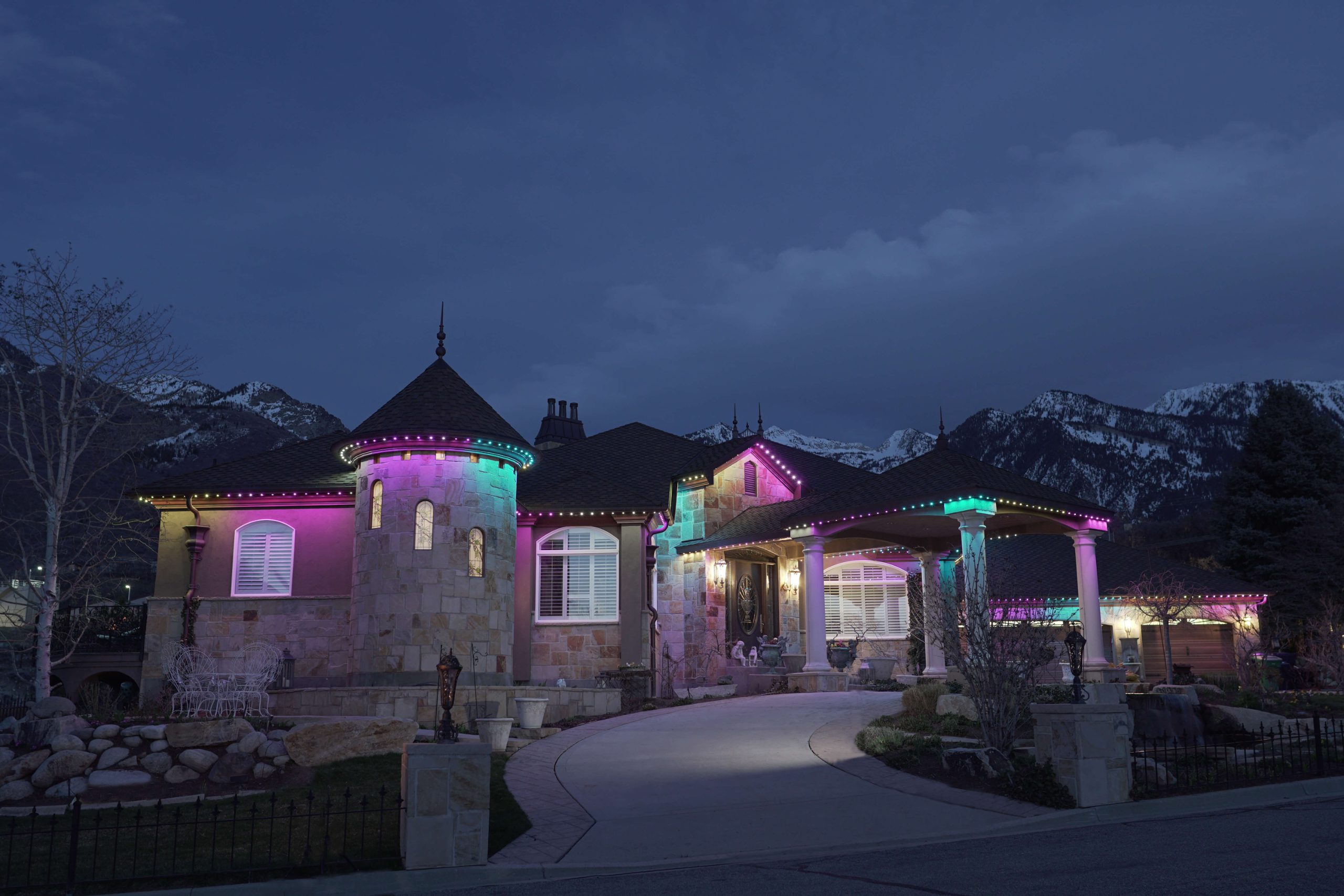 Stone home with multicolor permanent roofline lights at dusk